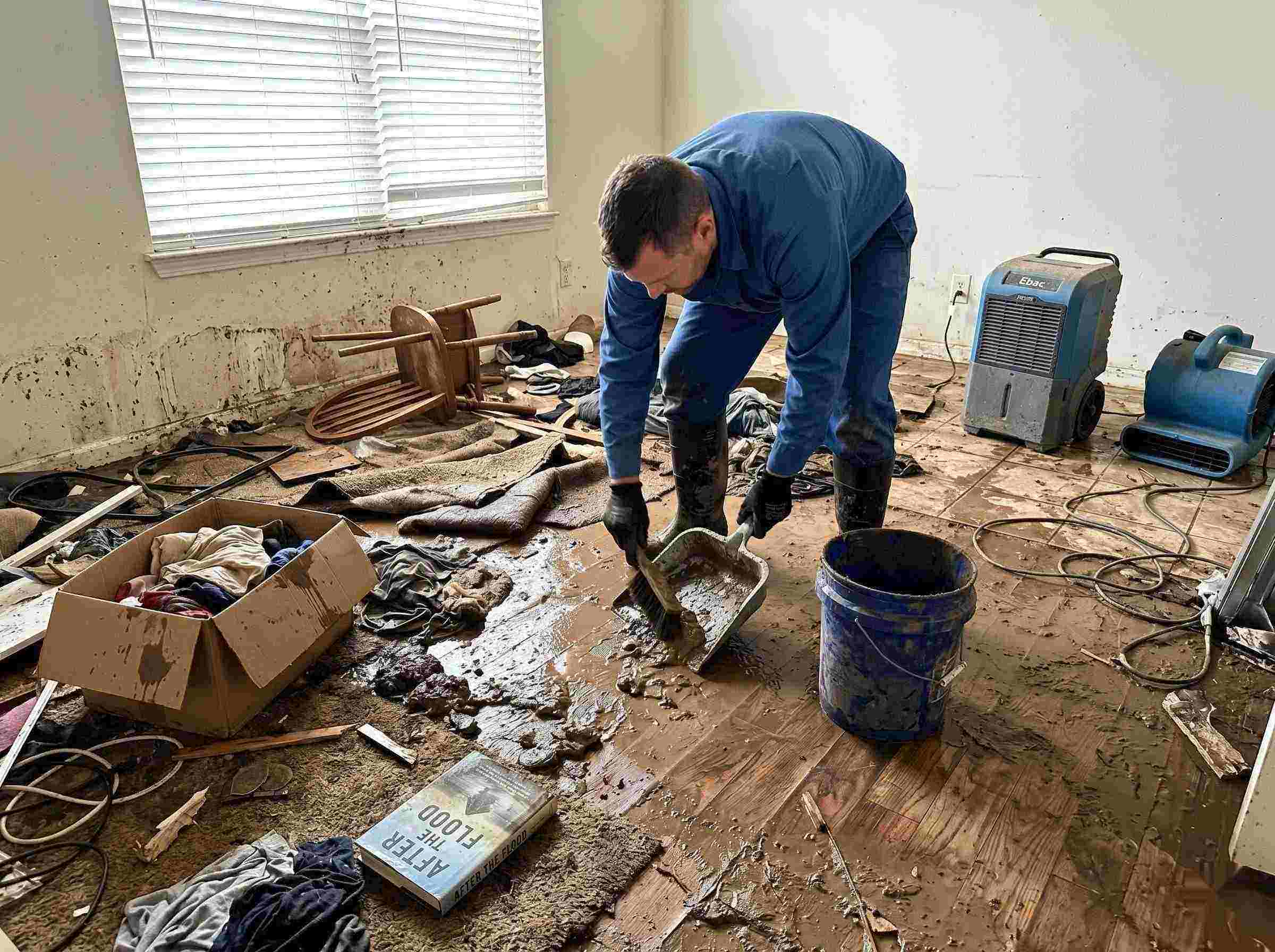 Realistic photo of a technician performing mud and debris removal after a home flood in Irvine, showing soaked furniture, wet flooring, and scattered debris during post-flood cleanup.