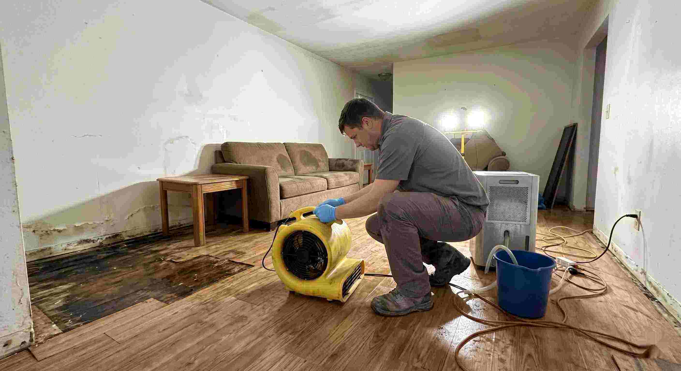 Professional water damage restoration technician drying wet floors with equipment during cleanup process in Corona